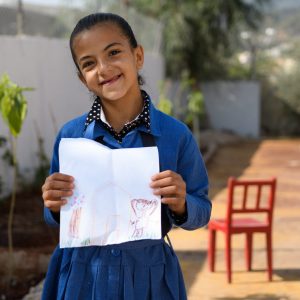 Young girl from Jerash refugee camp holds a self portrait drawn in crayon