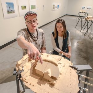 Kyle Singer and Emily Sullivan point to a detail on one of David Brooks' fracking-inspired art pieces
