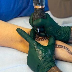 Closeup of Lambert tattooing a snake on his client's forearm