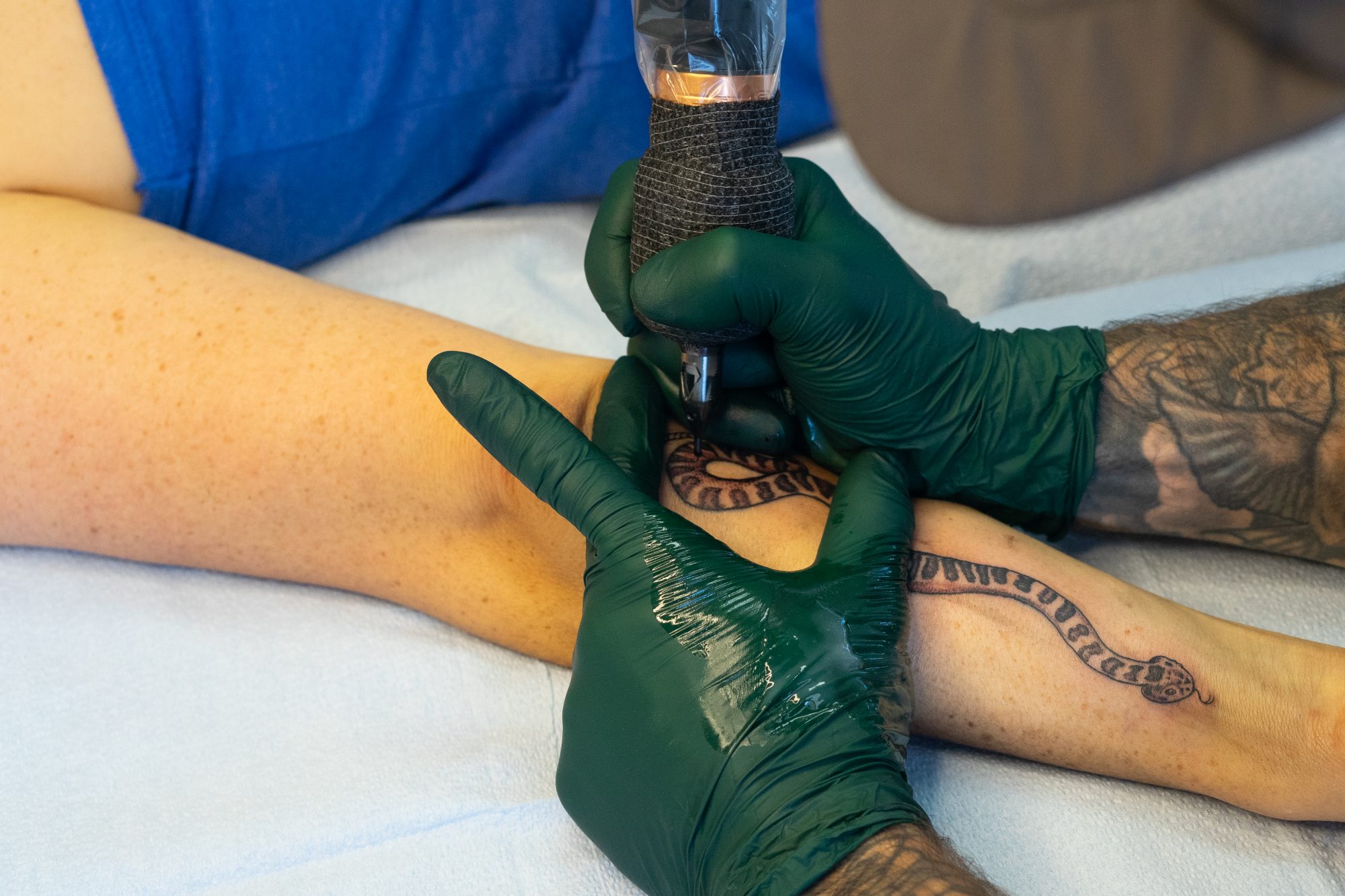 Closeup of Lambert tattooing a snake on his client's forearm