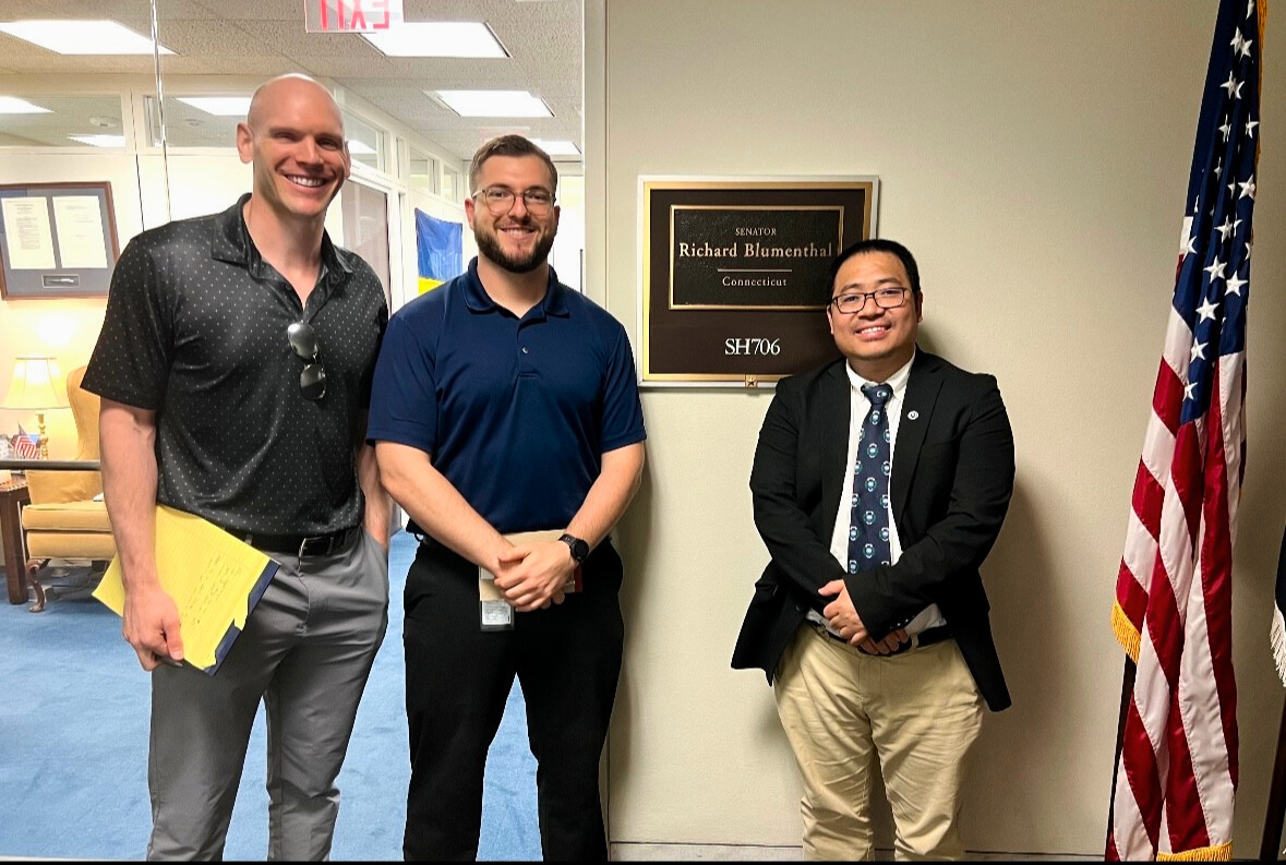 Justin Frigault posing with colleagues next to a plaque denoting Senator Richard Blumenthal's senate office in Washington DC