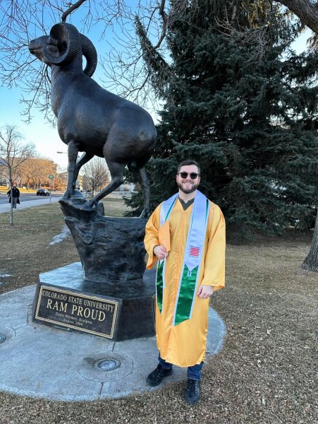 Justin Frigault wearing Gold regalia at his CSU graduation in 2023. He poses next to a Ram statue outside Moby Arena.