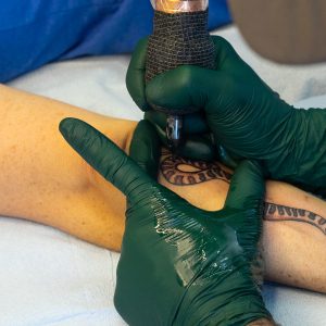 Closeup of Lambert tattooing a snake on his client's forearm