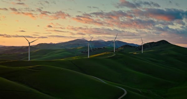 Aerial photograph of green hills in Altamont, California. The hills are dotted with windmills.