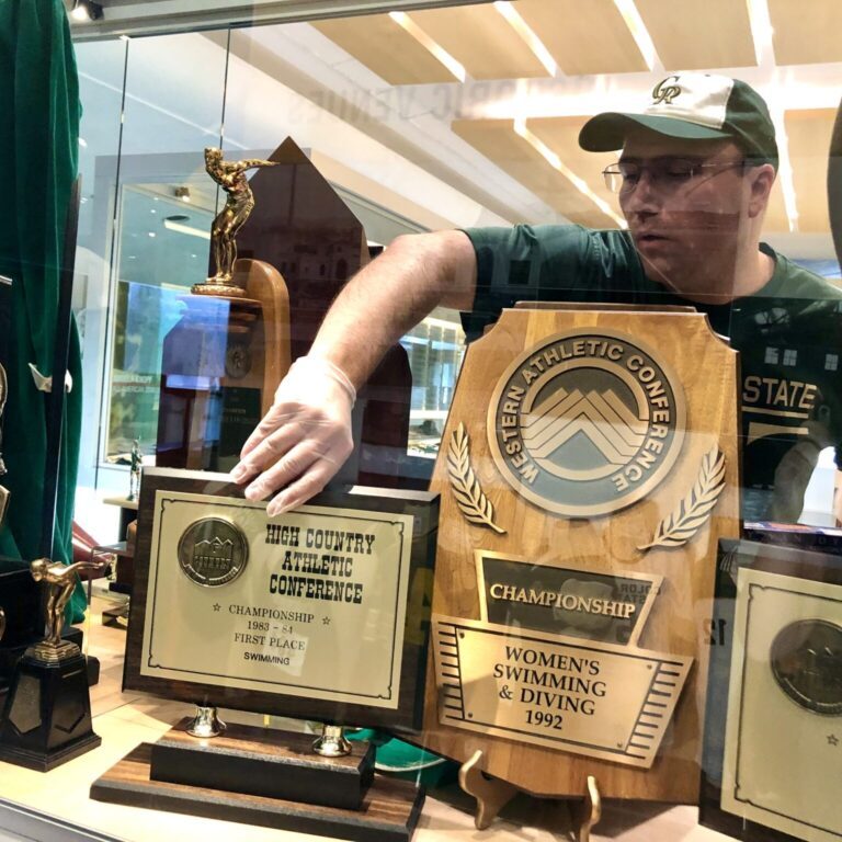 John Hirn curating CSU athletics trophies in a display case at Canvas Stadium